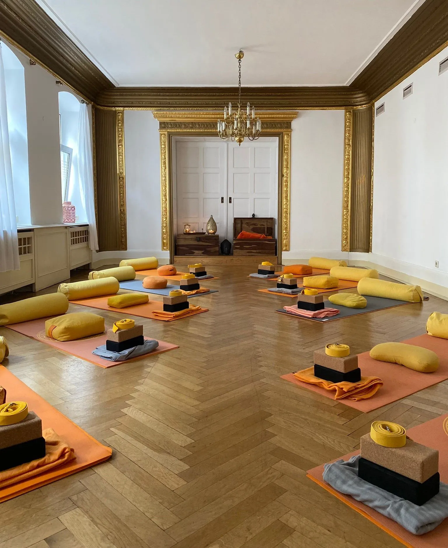 Yogaraum der YogaLounge: Fischgrätparkett, Kronleuchter und vorbereitete Matten mit Kissen und Blöcken